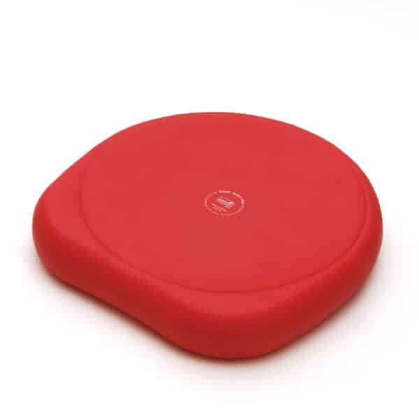 A red Sissel sitfit plus cushion. It has a slightly different shape to it that the SitFit which is circular. This inflatable cushion has a flat sitting surface. One side is circular and the opposite side has contours where your thighs would sit. It is more stable when you sit on it that way round. In the centre is the Sissel logo and the name of the product stamped in white print. The detail around the logo is in a circle.