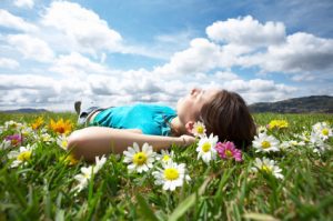 Image of beautiful sky with clouds and plants in the grass with someone lying on their back enjoying the sun for a blog about the health benefits of walking