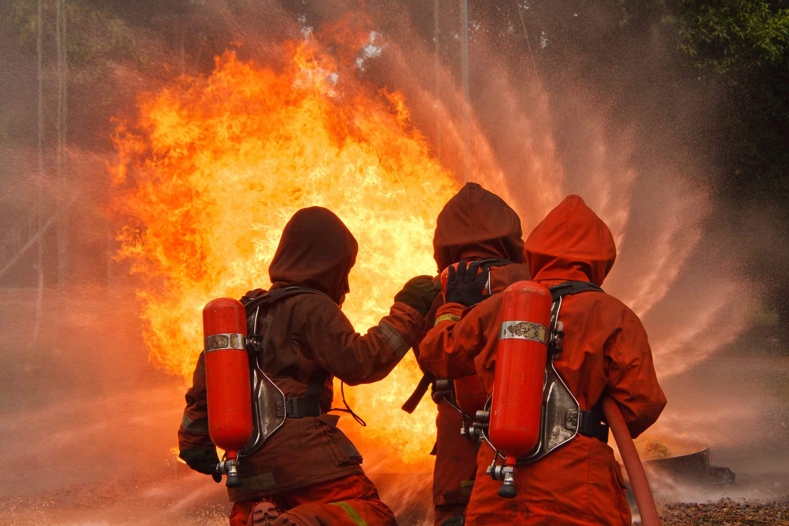 Three firefighters are stood next to each other holding a hose to put out a raging fire. This image is to depict inflammation.