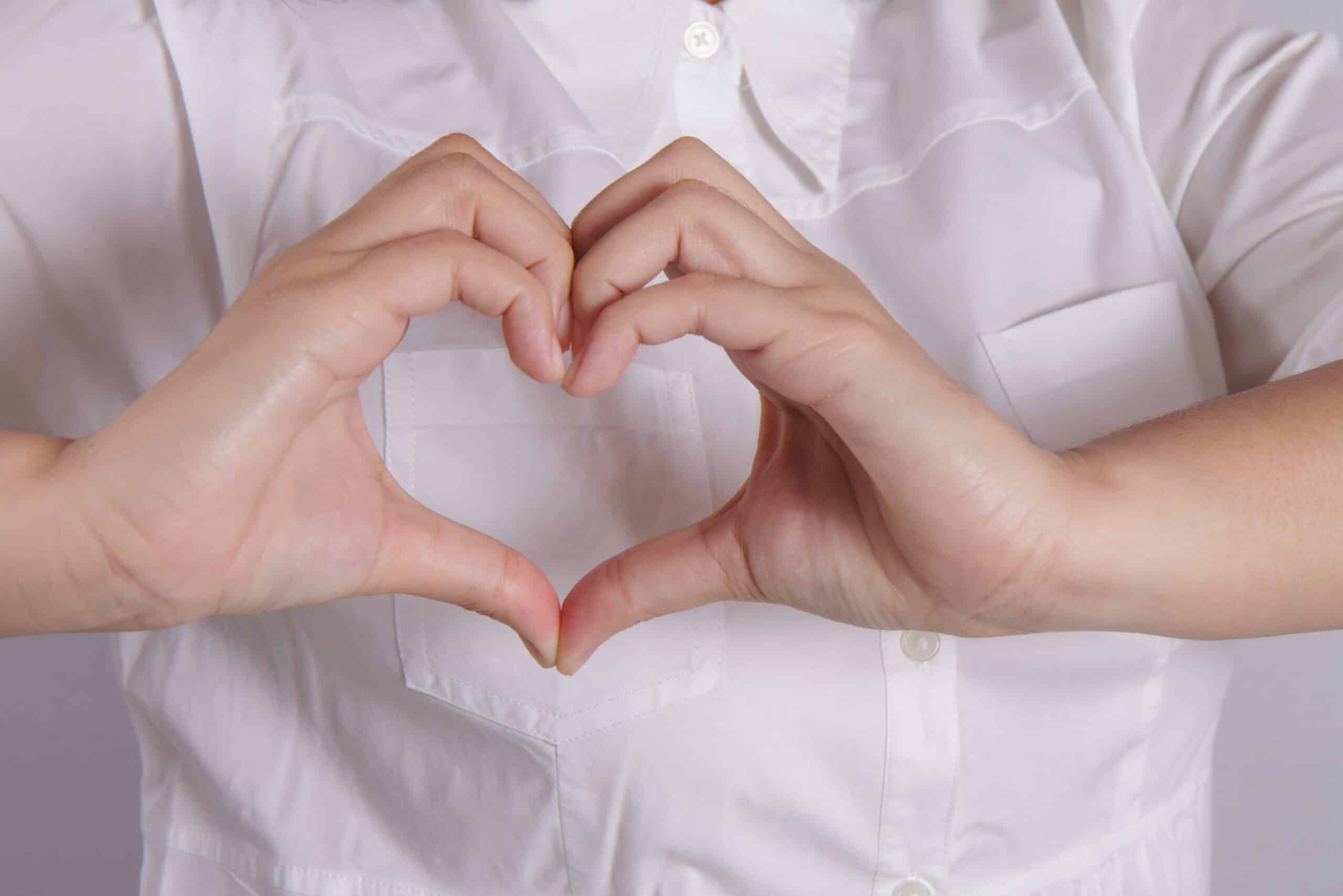 A zoomed in image of someone wearing a white blouse and holding their hands in a heart shape.
