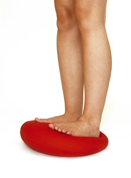 You can just see a bare pair of legs from the knees down. This person is stood on a red SitFit balancing. From the angle they are on the SitFit it looks like they have more weight into their heels.