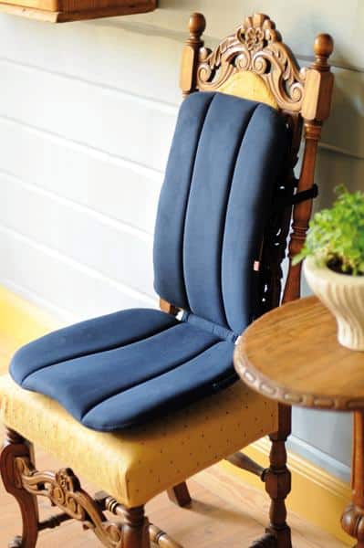 A blue Sissel full dorsaback placed on top of an ornate high backed dining room chair. You can see the contours to support your legs and lower back.