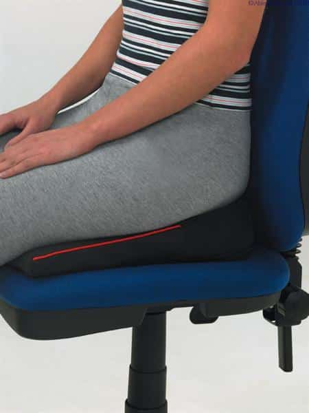 A lady wearing grey leggings and a striped top is sitting on a Harley designer wedge which is place on a standard blue office chair. The image is zoomed in so you can only see her torso and arms which are on her lap. You can tell the designer range as they always have the red piping on the side which this blac wedge has in the picture.
