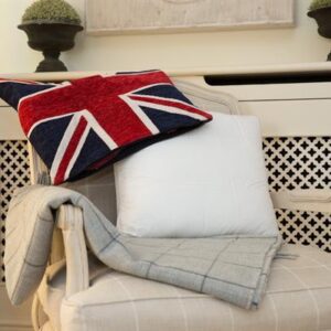 A homely scene. The background is cream as there is the deep chair, the fabric of which has white stripes horizontally and vertically. Drapped over the back of the chair is a union jack cushion cover and leaning against the back of the chair is a Sittingwell back support for the sofa and deep chairs similar to the one it is displayed on. The Sittingwell cushion does just look like a white square - the inside of a cushion before the cover goes on, that's the magic of it, noone ever knows and your home looks as fab as ever.
