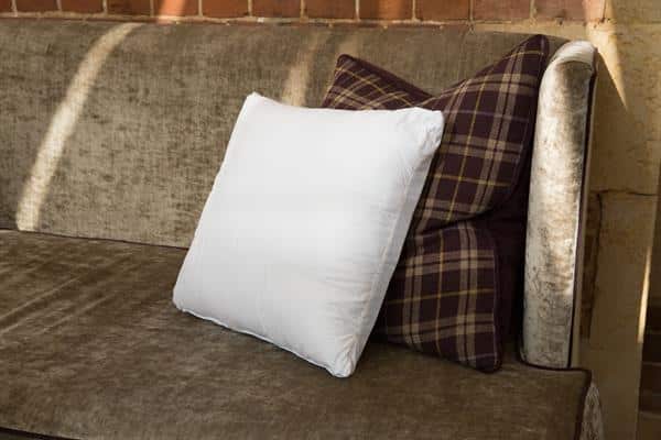 Placed in front of a purple tartan sofa cushion on a velvet sofa is a Sittingwell back support cushion demonstrating how in keeping it looks in the home.