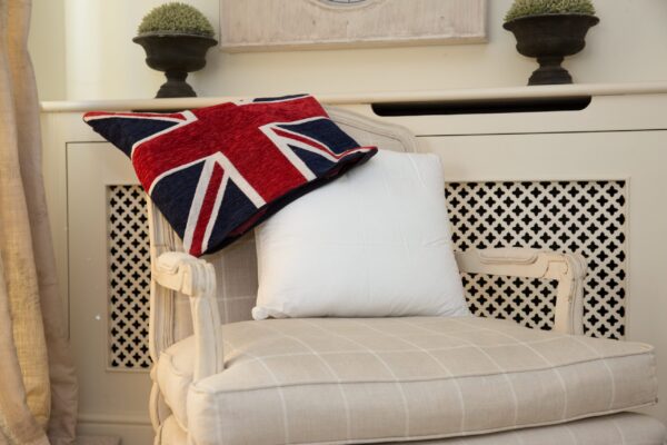A homely scene. The background is cream as is the deep chair, the fabric of which has white stripes horizontally and vertically. Drapped over the back of the chair is a union jack cushion cover and leaning against the back of the chair is a Sittingwell back support for the sofa and deep chairs similar to the one it is displayed on. The Sittingwell cushion does just look like a white square - the inside of a cushion before the cover goes on, that's the magic of it, noone ever knows and your home looks as fab as ever
