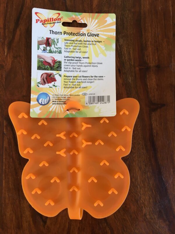 A photo of the underside of an orange Papillon Thorn Protection glove. It is made from malleable plastic which has raised areas of plastic for grip it is shaped like a butterfly. It has a label above giving the name of the product and a series of photographic examples of someone using it.