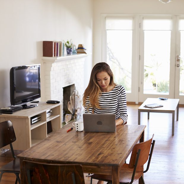 A lady sat working on her laptop at her dining room table. Relieve-Back-Pain-Working-From-Home