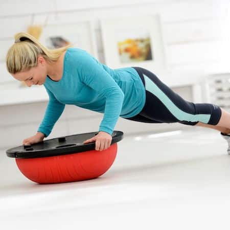 A lady in a press up position with her hands either side of the fit dome balance trainer. The dome is red and she has it upside down so that her hands are either side of the flat base to balance and hold herself steady.