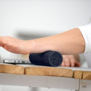 Close up of a womans arm using the Sissel Myofascial Release Mini Roller by rolling it on her wodden desk with her forearm to massage that area
