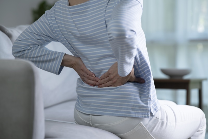 Old scar casuing back pain Woman sat on her sofa holding and arching her back to depict old scars can cause back pain